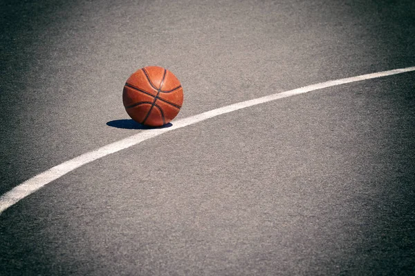 A basketball ball lies on the asphalt outside the white line.