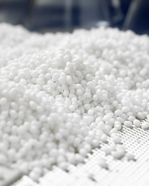 Mavi arka plandaki bir laboratuarda beyaz plastik bir polimer granülün dikey yakın çekimi.