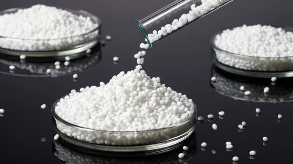 Closeup of a white plastic polymer grain is poured in petri dishes on a dark background. Conceptual image.