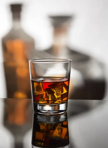 Whiskey with ice against a background of two bottles — Stock Photo, Image