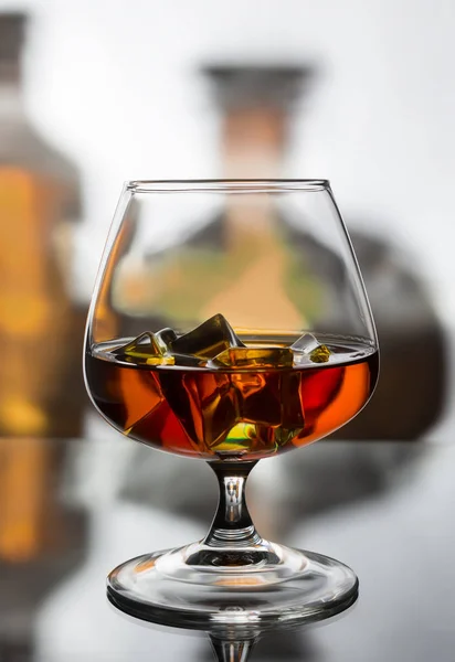 A glass of cognac with ice against the background of two bottles — Stock Photo, Image