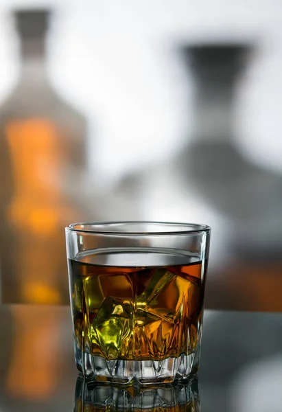 A glass of whiskey with ice against the background of bottles — Stock Photo, Image