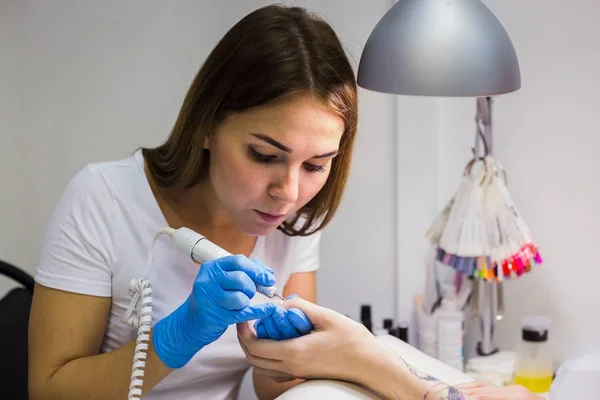 Donanım manikür bir salonda. Manikürcü elektrik törpü matkap uyguluyor