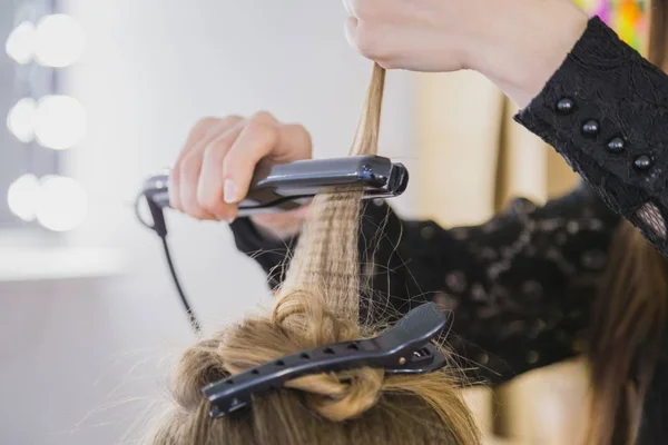 Close up of stylist hands with styling iron straightening woman hair — Stock Photo, Image