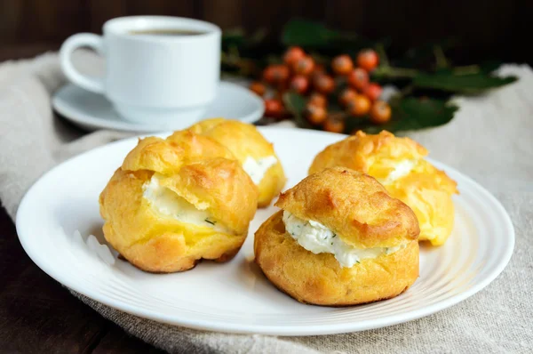 Bollos recién horneados eclairs rellenos con queso cottage picante y una taza de café (espresso) sobre un fondo de madera oscura. Desayuno ligero . — Foto de Stock