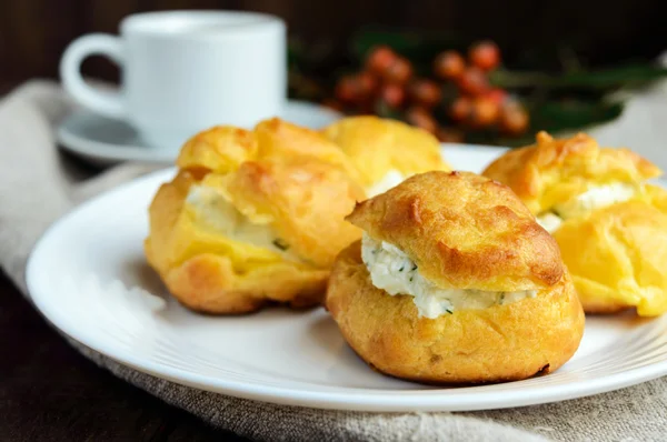 A frissen sült zsemlék eclairs fűszeres túróval töltve és egy csésze kávé (eszpresszó) sötét fából készült háttéren. Reggeli. Közelről — Stock Fotó