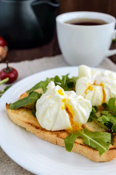 Œufs cuits dans un sachet (pochés) sur du pain grillé et des feuilles vertes croustillantes de roquette et une tasse de thé. Petit déjeuner diététique . — Photo