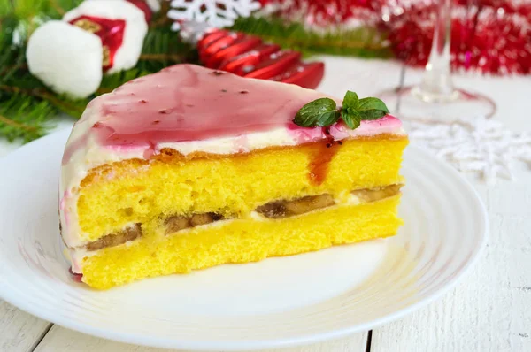 Sponge cake with a layer of banana, milk cream and cranberry syrup on a white background. Holiday dessert. Christmas theme. — Stock Photo, Image