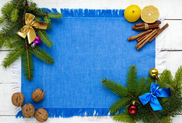 Fondo de Navidad. Abeto ramificado decorado con decoraciones coloridas, nueces, canela, limón sobre una servilleta azul sobre un fondo blanco. La vista superior . — Foto de Stock