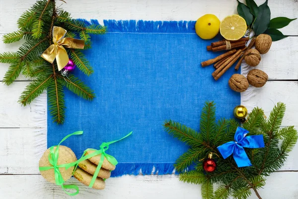 Fondo de Navidad. Abeto ramificado decorado con decoraciones coloridas, galletas de limón, nueces, canela, cítricos en una servilleta azul sobre un fondo blanco. La vista superior . — Foto de Stock
