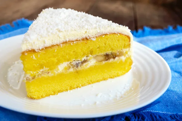 Gâteau éponge doux avec couche de banane crémeuse, saupoudrer de noix de coco sur le dessus. Option dessert festif. Gros plan . — Photo