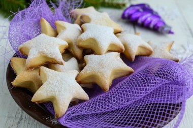 Homemade vanilla cookies in star-shaped decoration with powdered sugar on a purple napkin. Close up clipart