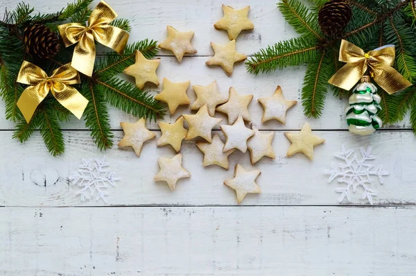 Zelená jedle větve a dekorace zlaté mašle a soubory cookie ve tvaru hvězdy na bílém podkladu. Vánoční téma. Pohled shora. — Stock fotografie