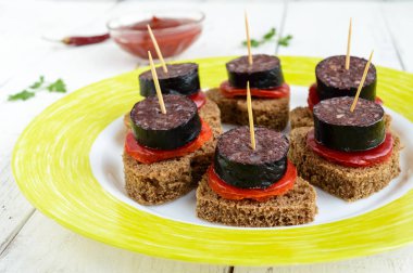 Siyah çavdar ekmeği bir kalp, kan sosisi (Morcillo) ve şiş üzerinde sweet pepper ve domates sosu Beyaz ahşap zemin üzerinde parçalar şeklinde sandviçle