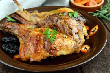 Koyu ahşap zemin üzerine seramik bir tabakta kuru erik ile kavrulmuş tavşan bacak. Yakın çekim. Tatil menü. Paskalya, Noel.