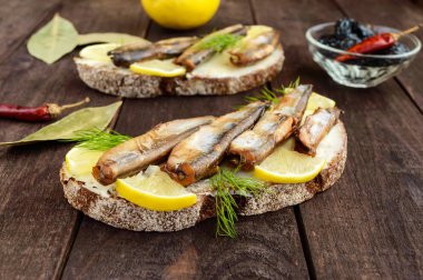 Füme balık capelin (hamsi), limon siyah siyah ekmek üzerinde sandviç. Koyu ahşap bir masa üzerinde snack.