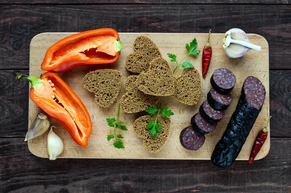 Morcillo (Spanish black pudding, blood sausage), cutting slices, black rye bread in a heart shape, pepper, garlic on a wooden board.