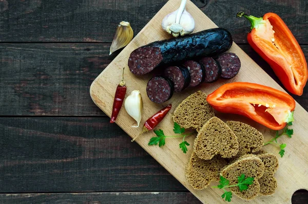 Morcillo (spanischer Blutwurst, Blutwurst), Scheiben schneiden, Schwarzbrot in Herzform, Pfeffer, Knoblauch auf Holzbrett. — Stockfoto