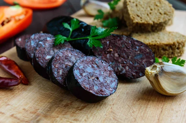 Morcillo (Spanish black pudding, blood sausage), cutting slices, black rye bread in a heart shape, pepper, garlic on a wooden board.