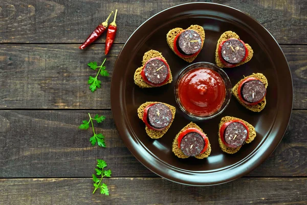 Sandwiches con pan de centeno negro en forma de corazón, salchicha de sangre (Morcillo) y trozos de pimiento dulce en pinchos en un tazón de cerámica —  Fotos de Stock