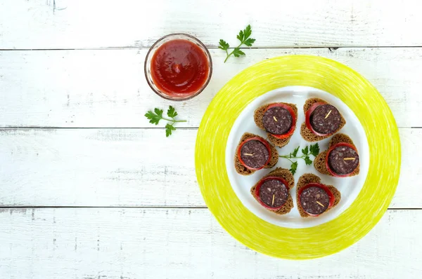 Broodjes met zwarte roggebrood in de vorm van een hart, bloedworst (Morcillo) en pieces of sweet pepper op spiesjes en tomatensaus, op een witte houten achtergrond — Stockfoto