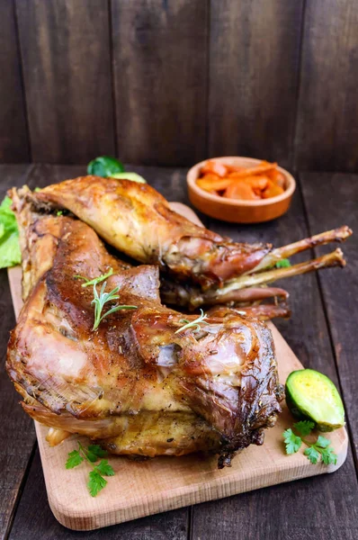 Ganze Kaninchen auf einem Holzbrett mit gebackenen Möhren und Rosenkohl auf dunklem Hintergrund braten. ein festliches Essen. — Stockfoto