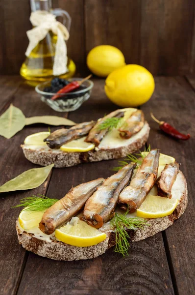 Sandwich met gerookte vis lodde (sprotten), citroen op Zwarte roggebrood. Snack op een donkere houten tafel. — Stockfoto