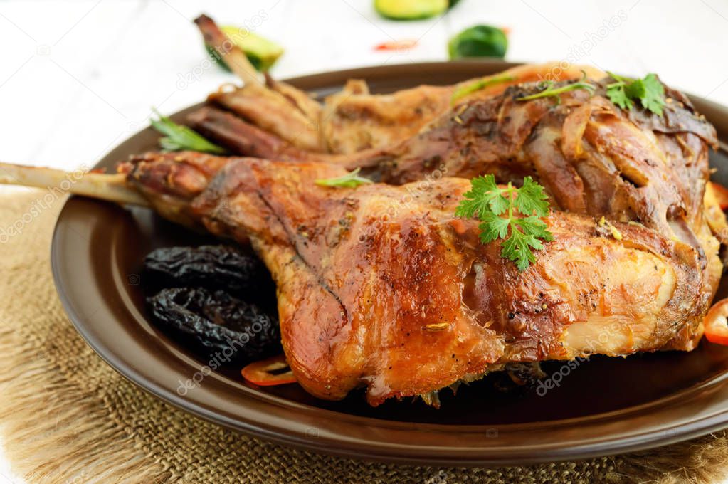 Roasted rabbit leg with prunes on a ceramic plate on light background. Close up. Holiday menu. Easter, Christmas.