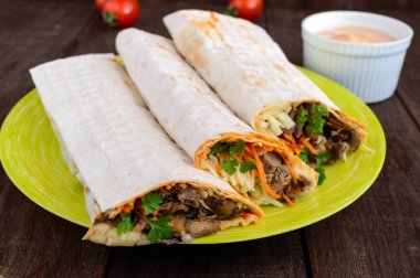 Shawarma sandviç - taze rulo dolu ızgara et, mantar, peynir, lahana, havuç, sosu, yeşil ile ince silindir Mini değirmenler (pita ekmeği). Geleneksel Doğu aperatif. Koyu ahşap arka plan üzerinde.