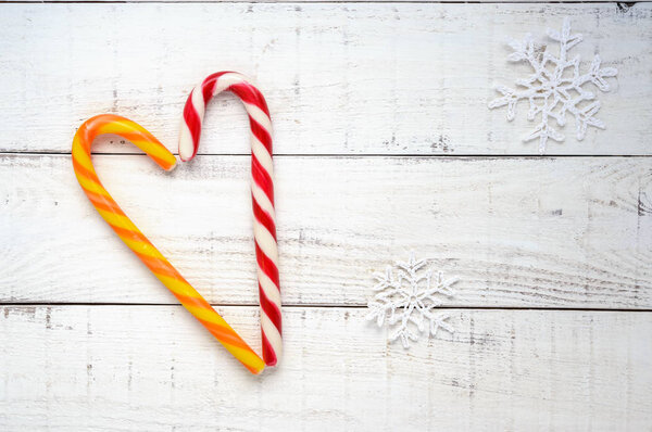 Christmas treats: bright candy canes, in a heart shape  on white a wooden board. The top view. Celebratory background.