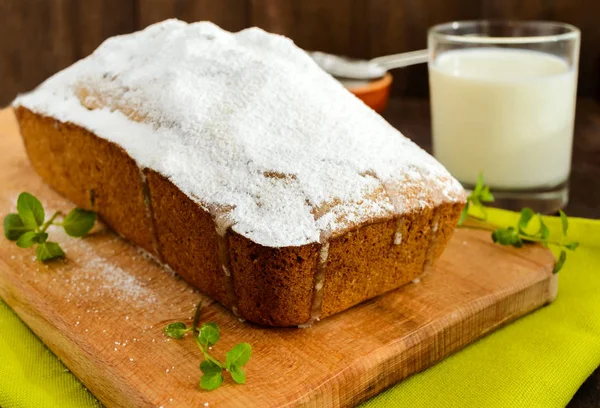 Pastel de frutas casero recién horneado, decorando la parte superior con azúcar en polvo en una tabla de cortar con un vaso de leche . — Foto de Stock