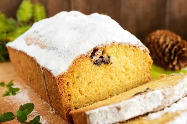 Свежеиспеченный домашний торт из буханки, украшающий верх сахарной пудрой на разделочной доске и зелеными ветвями ели и конусов . — стоковое фото