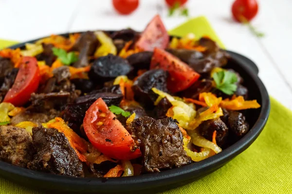 Trozos de pato asado, ganso (carne, hígado, corazón) con verduras (cebolla, zanahoria, tomate), con especias en una sartén redonda de hierro fundido en una servilleta verde. De cerca. — Foto de Stock