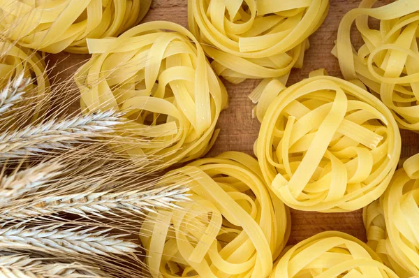 Pasta tagliatelle in the form of nests on a cutting board with spikelets of wheat. The top view. — Stock Photo, Image