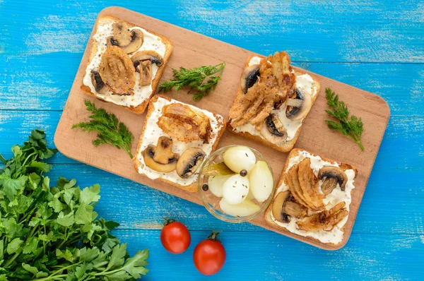 Pão branco torrado crocante na forma de um quadrado com cogumelos, cebolas, batatas fritas, molho tártaro em uma tábua de corte em um fundo de madeira azul. A vista superior — Fotografia de Stock