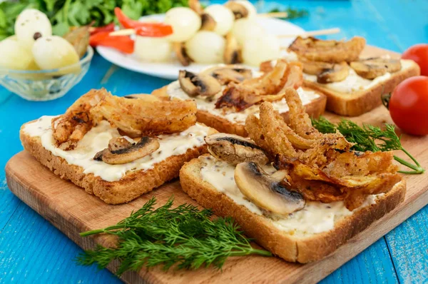Pão branco torrado crocante na forma de um quadrado com cogumelos, cebolas, batatas fritas, molho tártaro em uma tábua de corte em um fundo de madeira azul — Fotografia de Stock