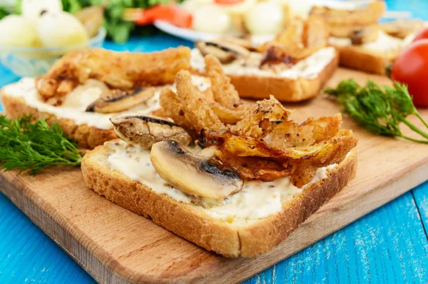 Crispy tosty biały chleb w kształcie kwadratu z pieczarkami, cebulą, frytki, sos tatarski na pokładzie cięcia na niebieskim tle drewnianych. — Zdjęcie stockowe