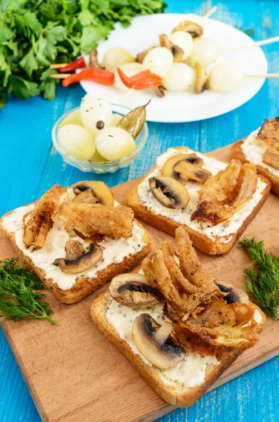 Pan blanco tostado crujiente en forma de cuadrado con setas, cebollas, papas fritas, salsa tártara en una tabla de cortar sobre un fondo de madera azul . — Foto de Stock