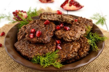 Beyaz ahşap zemin üzerinde bir seramik tabak üzerine nar taneleri ile sulu karaciğer pirzola. Yakın çekim