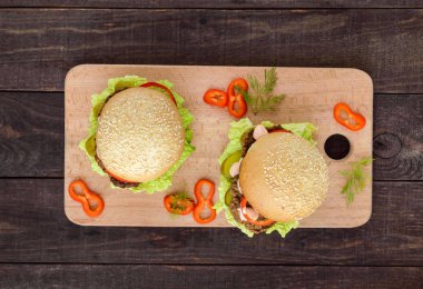 Karaciğer pirzola, domates, turşu, marul, baharatlı sos ve susam bir koyu ahşap arka plan üzerinde bir kesme tahtası üzerinde ile yumuşak bir topuz ile hamburger. Üstten Görünüm.