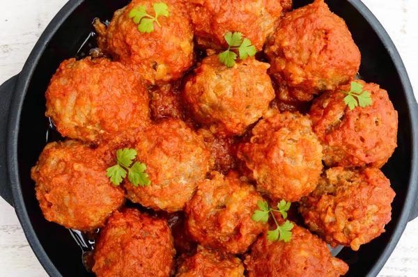 Meat balls in spicy tomato sauce served on a cast iron pan on a white wooden background. The top view. Close up — Stock Photo, Image