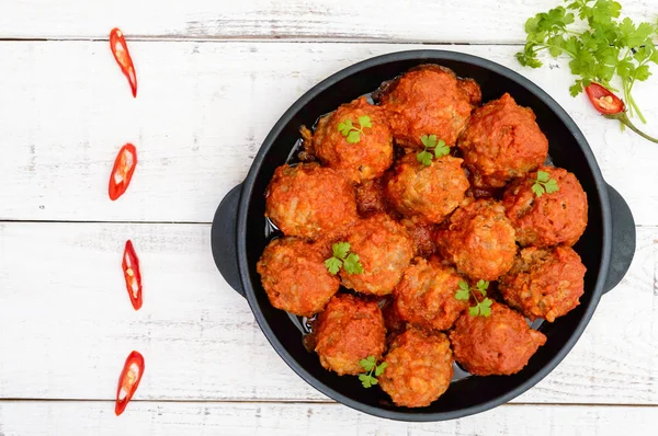 Meat balls in spicy tomato sauce served on a cast iron pan on a white wooden background. The top view.