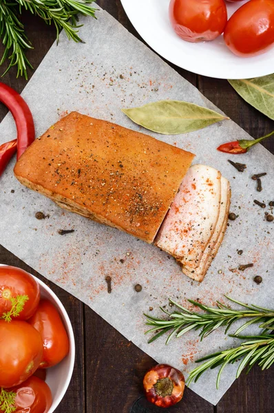 Ein großes Stück Speck gebacken mit Gewürzen und Kräutern auf einem Papier mit marinierten Tomaten. die Draufsicht. ein festliches Essen. Ostern. Weihnachten. — Stockfoto