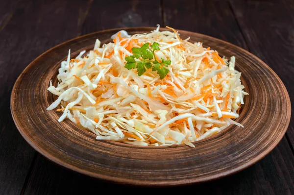 Salad of fresh cabbage and carrots in a clay bowl on dark wooden background. Lean vegetarian vitamin dish. — Stock Photo, Image