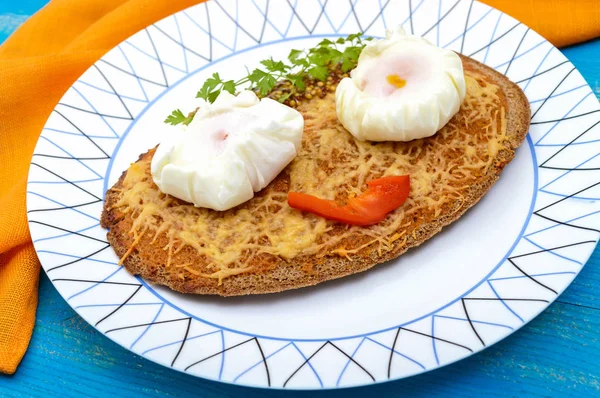 Детское меню: горячий сэндвич с черным ржаным хлебом с тертым сыром и яйцо-пашот на тарелке на синем деревянном фоне. Детская еда . — стоковое фото