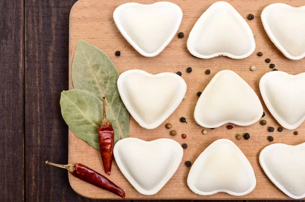 Uncooked dough in the shape of a heart (dumplings, ravioli, pelmeni), on a cutting board. Close up. The top view — Stock Photo, Image