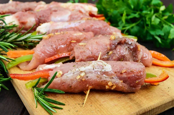 Неварені свинячі м'ясні рулети, фаршировані овочами (перцем, морквою) у гарячому часниковому соусі на обробній дошці. Сирий, напівфабрикат . — стокове фото