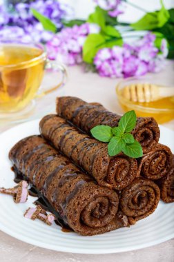 Haddelenmiş, ince narin çikolatalı krep bir yığın beyaz bir tabak ve Ballı bitkisel çay hazır. Dikey Görünüm