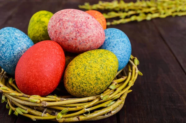 Farverige malede æg i en rede af kviste af pil på en mørk træbaggrund. Traditionelt til påske . - Stock-foto