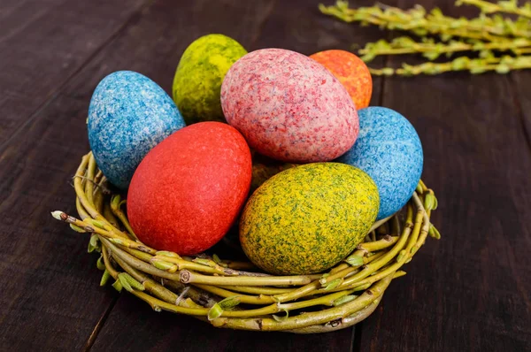Барвисті розписані яйця в гнізді гілочок верби на темному дерев'яному тлі. Традиційно на Великдень . — стокове фото